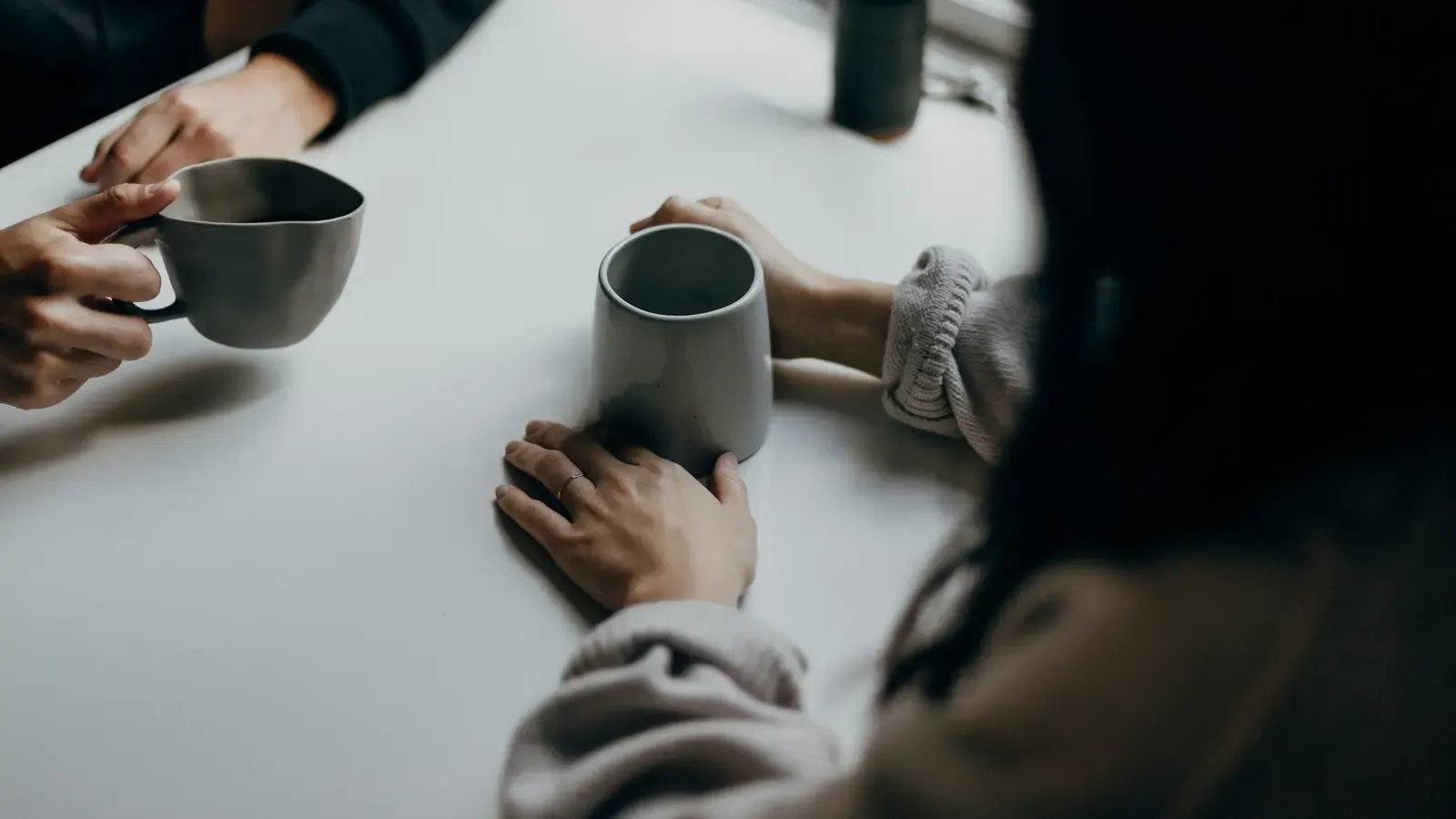 Duas pessoas sentadas à mesa segurando canecas durante uma conversa.